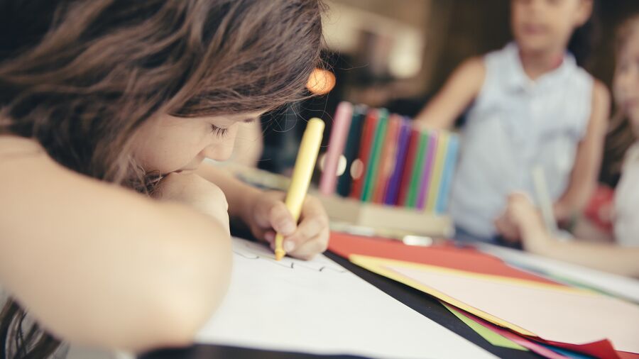 Barn tegner eller skriver liggende ind over bordet